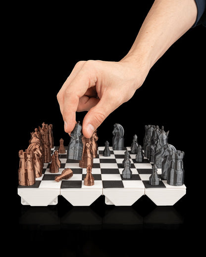 MJR Crafted 3D printed fold-up chess set with bronze and grey pieces on a black and white board. A hand is placing a grey knight.