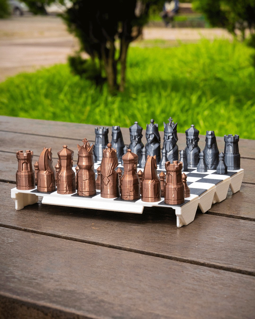 MJR Crafted fold-up chess set with bronze and grey 3D printed pieces on a white and black board, set on a wooden table.