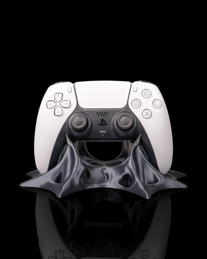 MJR Crafted modern sculptural gaming controller stand in dark grey PLA filament, holding a white PlayStation 5 controller.