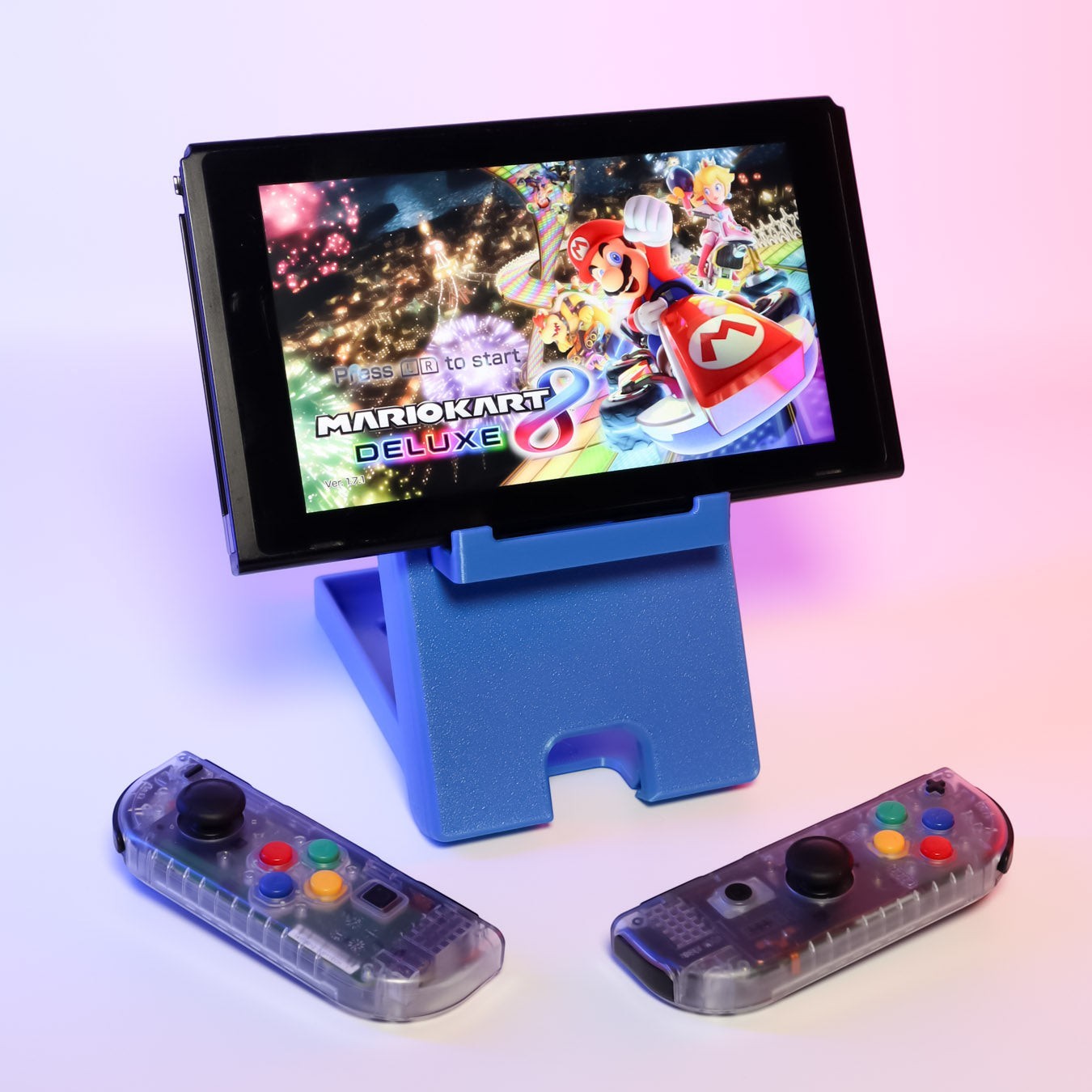 MJR Crafted blue 3D-printed foldable Nintendo Switch stand holding a Switch playing Mario Kart 8 Deluxe, with two clear Joy-Con controllers.
