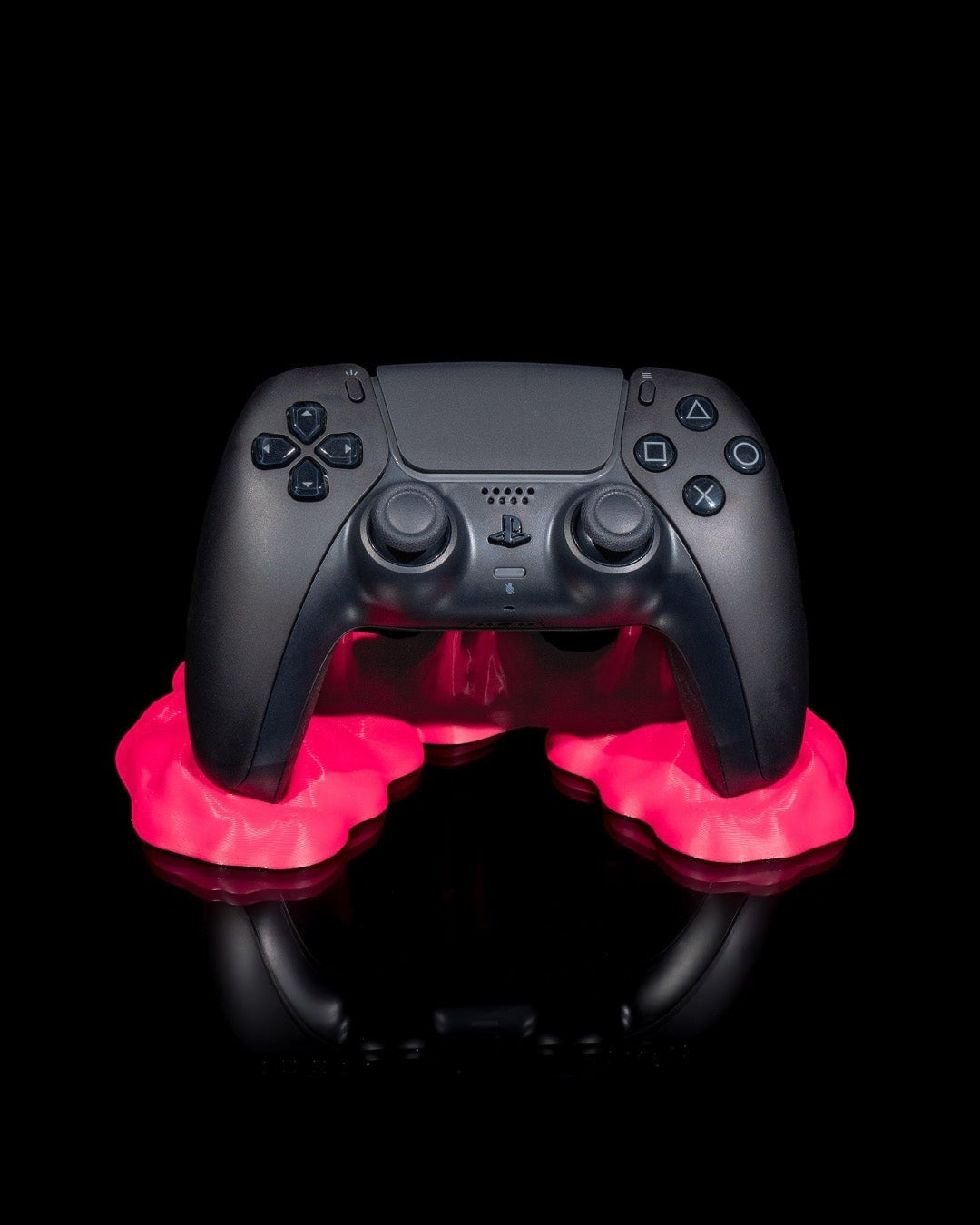 MJR Crafted black PS5 controller on a bright pink, blob-shaped stand against a black background.