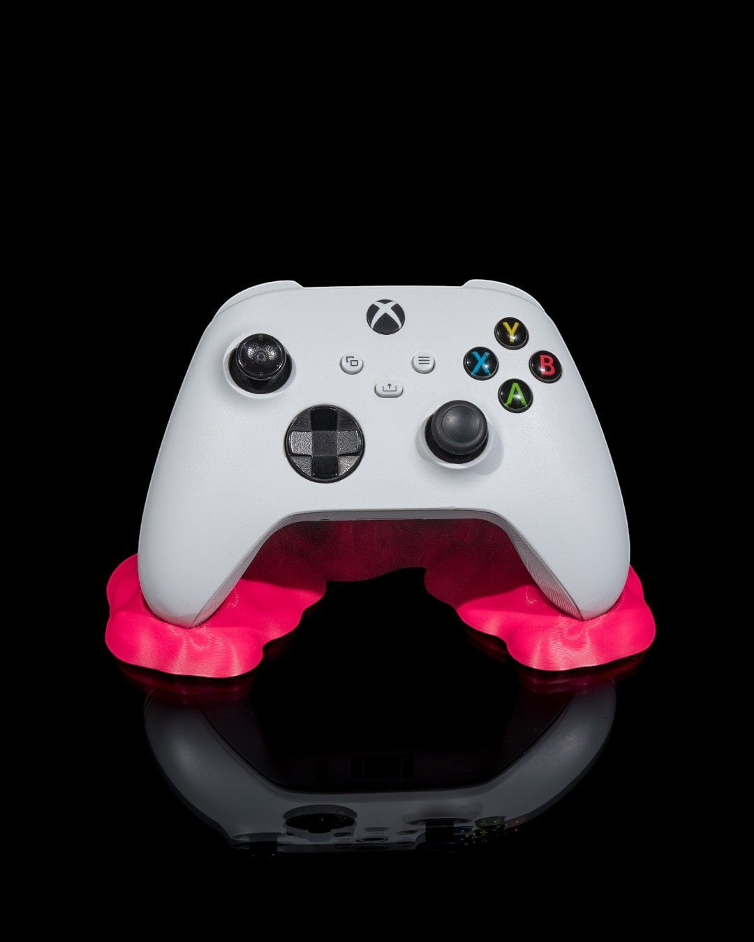 MJR Crafted white Xbox controller resting on a bright pink minimalist stand against a black background.