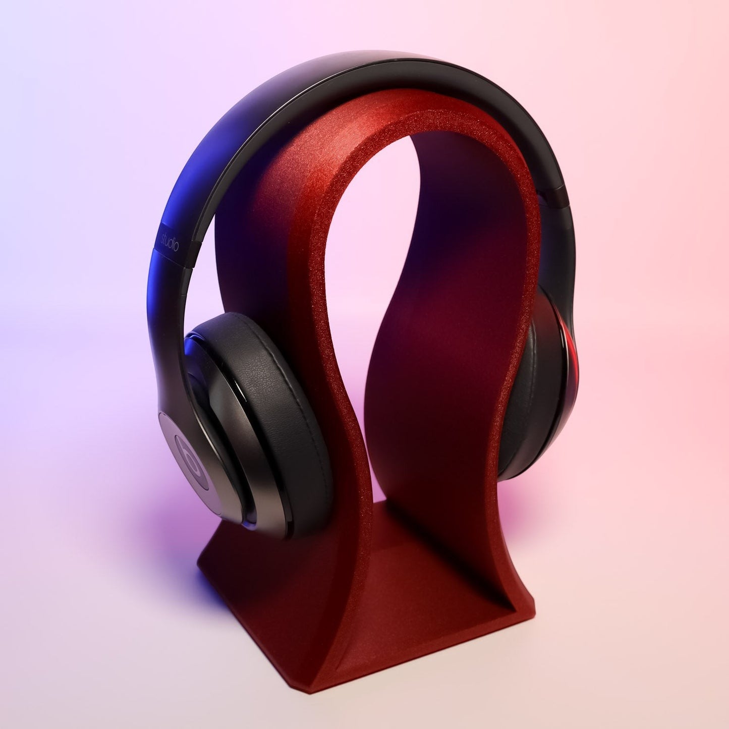 MJR Crafted sculptural headphone stand in deep red, holding black over-ear headphones. Modern, artistic design.