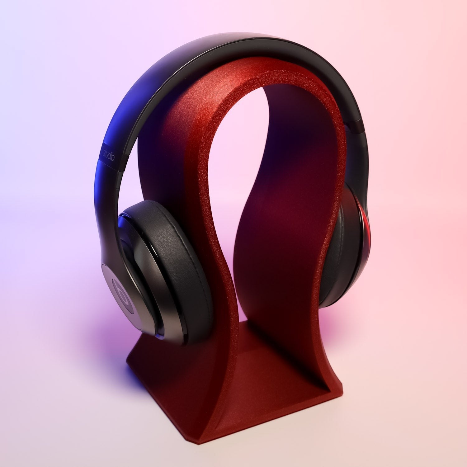 MJR Crafted sculptural headphone stand in deep red, holding black over-ear headphones. Modern, artistic design.