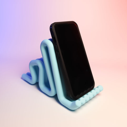 MJR Crafted light blue wavy phone stand holding a black smartphone. Modern desk accessory.