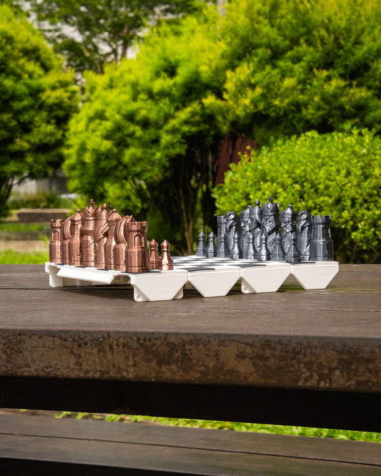 MJR Crafted Here fold-up chess set with bronze and silver 3D printed pieces on a wooden table outdoors.